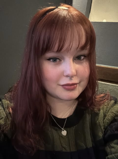 picture of Evie Gregory who has dyed dark hair and is wearing a green and black striped jumper